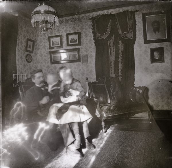Indoor portrait of a man sitting in a chair with a young girl? and two children sitting on his lap.