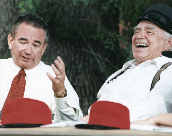 Tommy Thompson and Ernest Borgnine Wisconsin Governor Tommy Thompson, on the left, and actor Ernest Borgnine, on the right, sitting together. Thompson is gesturing with his hand and Borgnine is laughing. Two red baseball caps are on a table in front of the men.