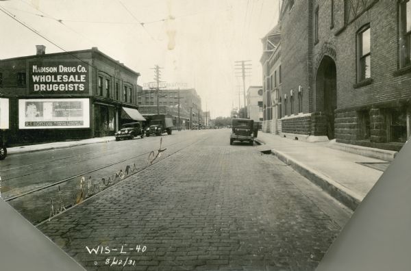Williamson Street View down Williamson Street, with Fauerbach Brewing Company on the right at 651-653 Williamson Street. The Madison Drug Company (Wholesale Druggists) and General Paper & Supply Company are both on the left side of the street. Several cars are parked along the curbs.