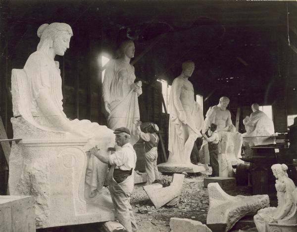 Carvers at work on the Karl Bitter sculpture for the fourth Wisconsin State Capitol (third in Madison). Between 1911 and 1913, a group of stone cutters (many of them Italian) worked on the four figural groups designed for the base of the dome. The figures were first carved near the Milwaukee Road shed and then hoisted into place when completed. Seen here are figures (left to right) faith, abundance, and three elements from strength.