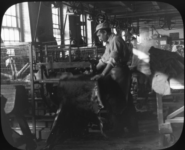 Interior view of the Pfister and Vogel Tannery, with a man working on leather at a machine.