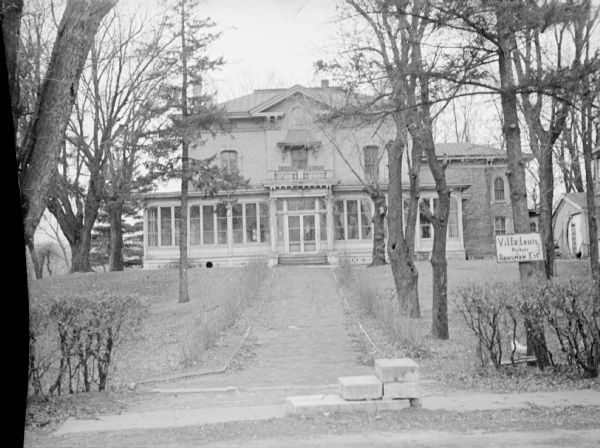 Villa Louis Before Restoration View of Villa Louis before restoration. A path leads up to an entrance. A tree in the foreground on the right has a sign that reads: "Villa Louis Historic Dousman Est."