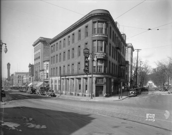 The Commercial National Bank building, on the corner of State and Carroll Streets, housed the bank as well as Mrs. Brown's Beauty Shoppe and Wegener and Roick Lawyers. On the right is a view down Carroll Street towards Lake Mendota. On the left down State Street among many other storefronts is the Palace Drug Store, the YWCA, and the marquee for the Orpheum Theatre.
