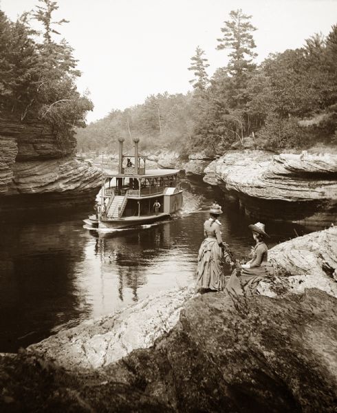 Elevated view of the "Dell Queen" entering the Narrows via Devil's Elbow as Hattie and Nellie Bennett look on from an overlook on the shoreline.