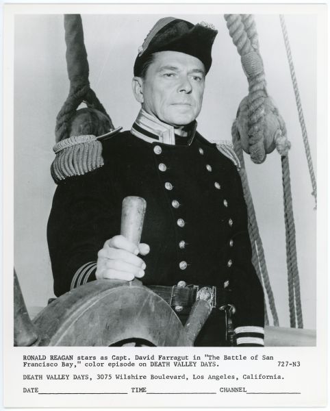 Ronald Reagan as Capt. David Farrgut in <i>Death Valley Days</i> Ronald Reagan wears a naval uniform as Capt. David Farragut in an episode of the TV show <i>Death Valley Days</i>. He stands behind and has one hand on a ship's wheel while looking down and to the right.