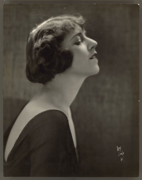 Helen Ferguson profile photograph Photograph in profile of actress Helen Ferguson. She wears a dark colored dress that shows part of her back and chest. Her face is pointed upward but is looking downward and her hair is cut in a bob.