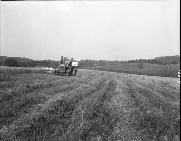 Man cutting and threshing with Case 9-foot combine at the University of Wisconsin Hill Farm.