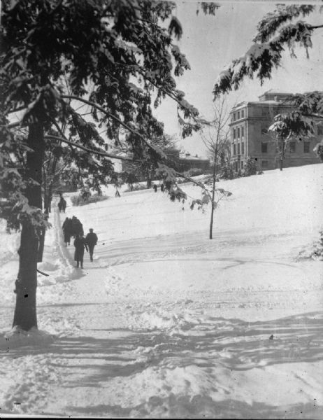 Winter scene showing students walking through snow near the Home Economics building. The University of Wisconsin Agricultural Hall is in the background.