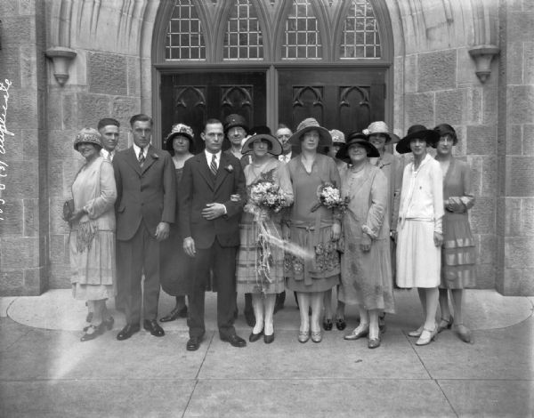 Mildred House and Lloyd Coleman wedding. The bride and groom are standing with guests in front of 1st Methodist Church, 203 Wisconsin Avenue.