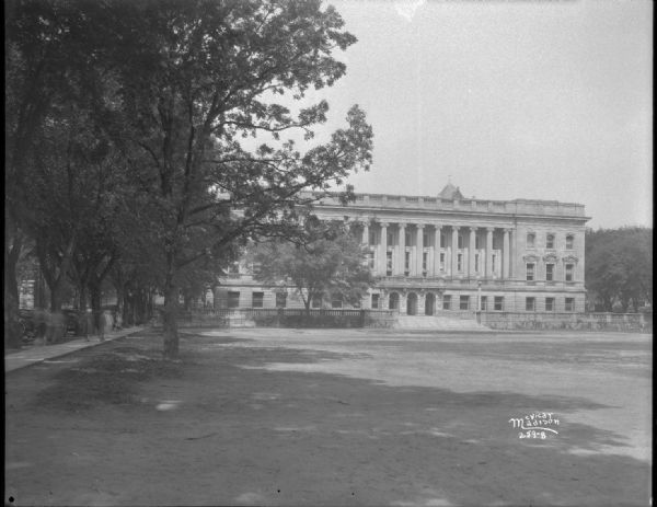 View across lawn towards the the front of the State Historical Society of Wisconsin and University of Wisconsin library at 816 State Street. Automobiles are parked along State Street on the left near a tree-lined sidewalk.