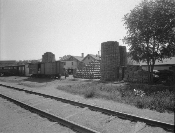 Loading barrels into a Chicago and Northwestern Railroad car behind the Hess Barrel Company (cooperage) at about 1950 Atwood Avenue. Stacks of oak barrel heads and staves are curing in the open air.