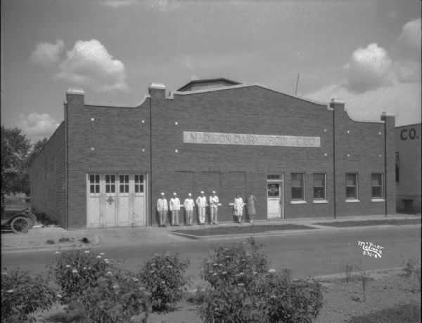 View across street towards the Madison Dairy Produce Building, with employees standing on the sidewalk in front of the building. Located at 1018 East Washington Avenue.