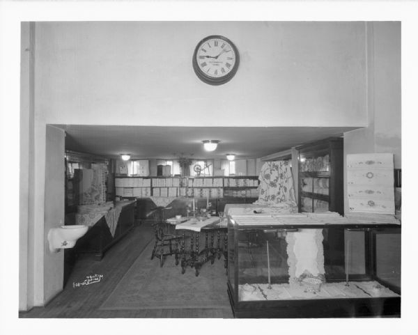 Kessenich's linen department. A clock is on the wall above the entrance, and a water fountain is on the wall on the left..