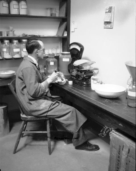 Man taking chemical CaCO4 out of a jar to measure it on Toledo Scale in Ricketts laboratory at Agriculture Chemistry Building, University of Wisconsin.
