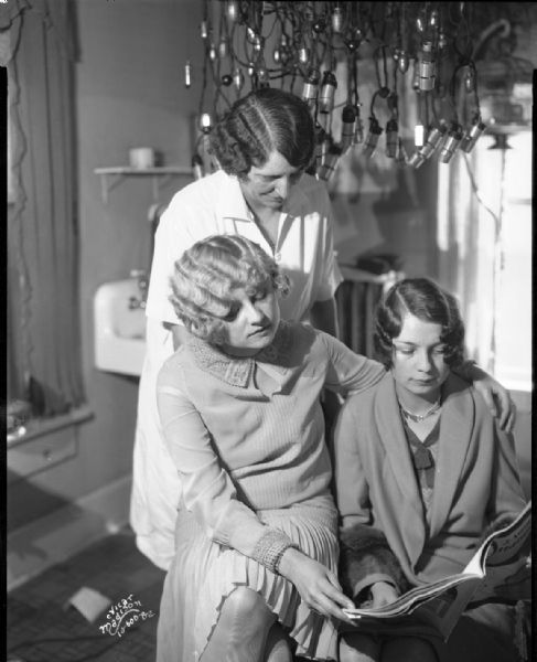 Three women (including American Girl — Miss Leeds and Miss Madison — Miss Rosenfeldt / Rosenthal) looking at "The American Hairdresser" magazine in the Rosemary Beauty Shop at 521 State Street.