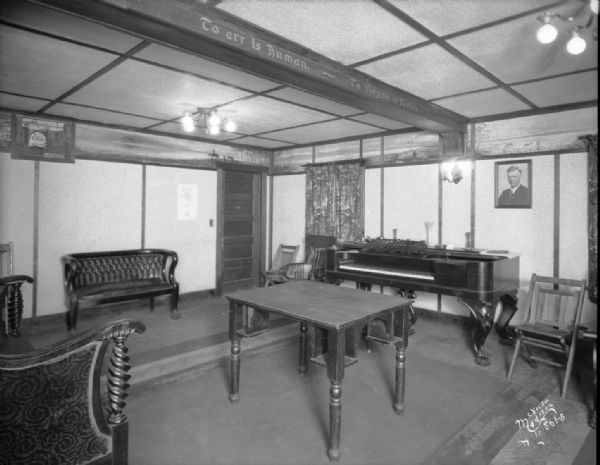Interior of Kilowatt clubhouse on Lake Monona. There is a piano along the back wall. A sign painted along a beam on the ceiling reads: "To err is Human — to Forgive is Divine."