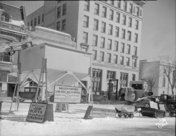 Wisconsin Foundry & Machine Company road equipment exhibit showing Badger portable sand gravel bins and pit-hoppers exhibited on Monona Avenue. The Garrick Theatre and Beaver Building (National Mutual Benefit Insurance) are in the background.