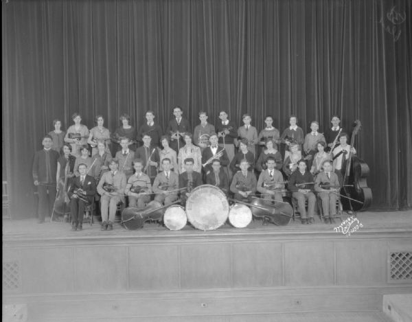 Group portrait of the East High School orchestra posing on a stage.