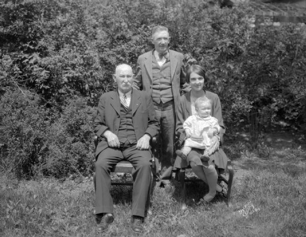 Oscar Romare four generations portrait. Two men, and a woman holding a baby, are posing outdoors.