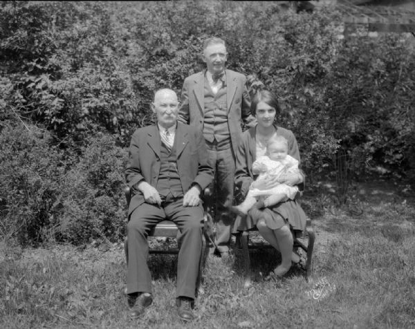Oscar Romare four generations portrait. Two men, and a woman holding a baby, are posing outdoors.