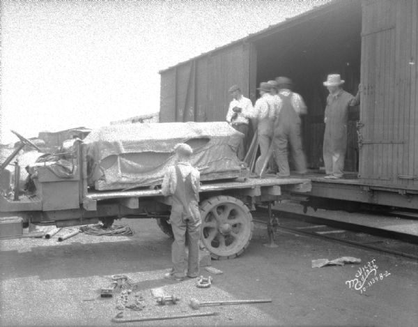 Five men are unloading a vault door from a railroad car onto a truck for the Bank of Wisconsin State Street Branch.