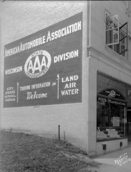 Close-up of the American Automobile Association (AAA) Wisconsin Division Headquarters display window, and a sign painted on the left side of the building at 715 University Avenue.