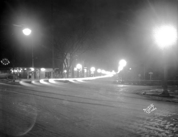 New street lights at night at the corner of S. Park Street, Vilas Avenue, and W. Washington Avenue. Looking south on Park Street. Mitchell's service station is on the left. There is a stream of lights from a moving car.