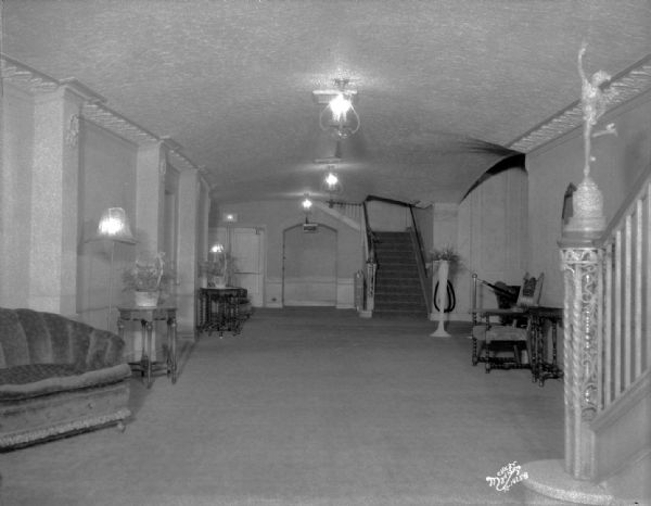 View of foyer from west end; Eastwood theatre, located at 2090 Atwood Avenue. On the right is a staircase and newel post with a statue of Mercury. Text on back of print reads: "Eastwood Theatre (opened Dec. 28, 1929) Foyer, showing stairways to the balcony, the aisle doors to the left and the inner lobby arch to the right."
