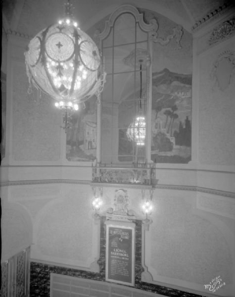 Elevated view of the Eastwood Theatre entrance lobby, showing details in the tower, including a large chandelier, and mirrored faux window, murals on the walls, and a lobby poster.
