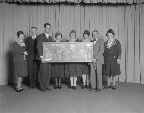 Group portrait of Dane county theater group champions on stage holding a painting.