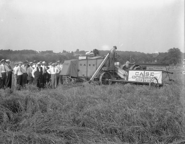 Two men operating Case 9-foot combine with a group of men observing, at University of Wisconsin Hill Farm.