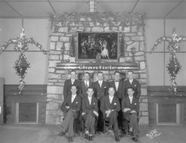 Group portrait of the Chanticleer orchestra and manager posing in front of the fireplace.