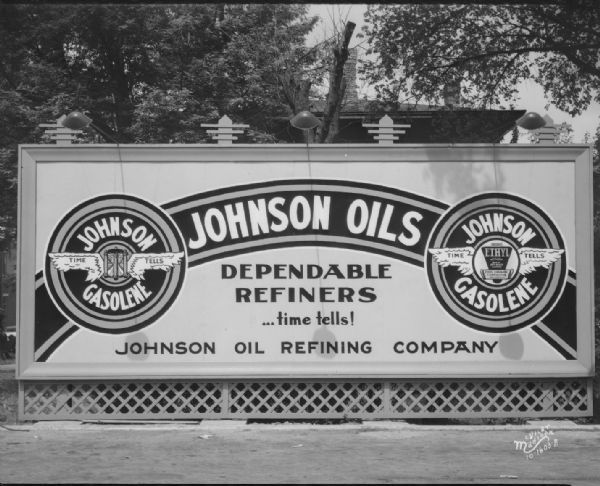 Johnson Oil Refining Company billboard. "Dependable refiners ... time tells!" Featuring 2 different logos for "Johnson Gasolene, Time Tells": the one on the left has an hourglass, and the one on the right reads "Ethyl."