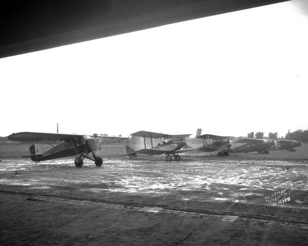 View from inside a building, perhaps a hangar, towards five airplanes, standing at starting line, at Madison Airport, Coolidge Avenue between North Street and Kedzie Street.