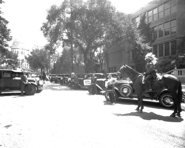 A man on a horse with Pontiac cars lined up on Wisconsin Avenue for the U.S. Indian Band parade, with the Wisconsin State Capitol in the background. They played a concert at the RKO Orpheum Theatre.