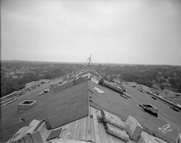 Elevated view of Novoid corkboard being installed on the roof of the new University of Wisconsin-Madison Field House, looking southwest. Men are working on the roof.