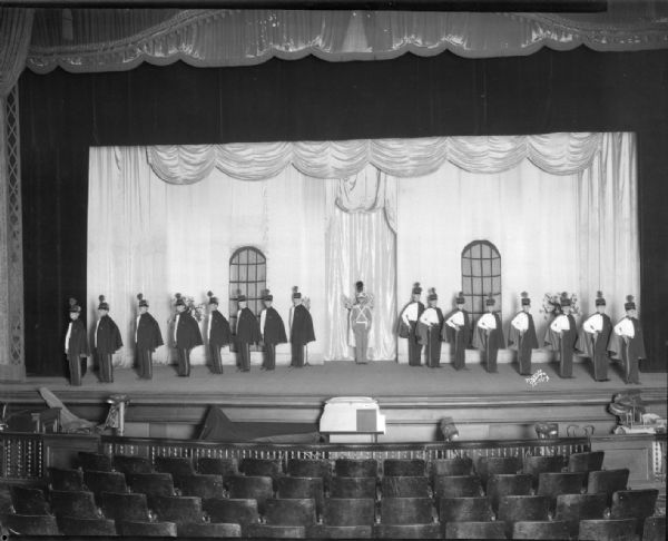 Floyd's Cadets (singers), a vaudeville act, in military uniforms standing in a "V" formation with hands on hips on stage at Orpheum Theatre. "First use of photo flash bulbs in Madison."