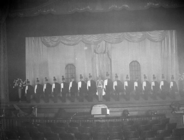 Floyd's Cadets (singers), a vaudeville act, in military uniforms standing in a line at the front of the stage at the Orpheum Theatre. "First use of photo flash bulbs in Madison."