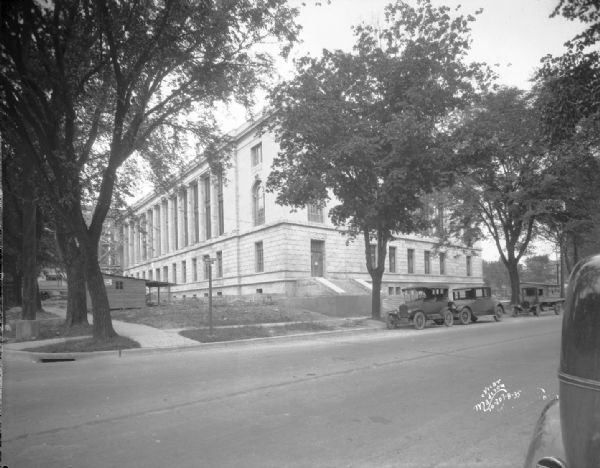 View looking north at front and side of U.S. Post Office and Courthouse from Wilson Street. Automobiles are parked along the curbs, and there is a construction shack in front of the building near the sidewalk.