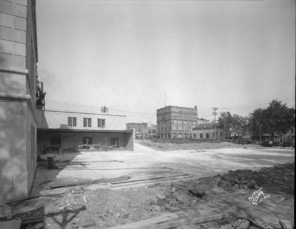 View looking north from rear parking lot and loading dock showing King Street Arcade, Cantwell Building, 121 South Pinckney Street, Riley Bremer Riley Oldsmobile dealership, 101 East Doty Street, and a Monona Tire Co. sign painted on the side of a building at 128 South Pinckney Street.