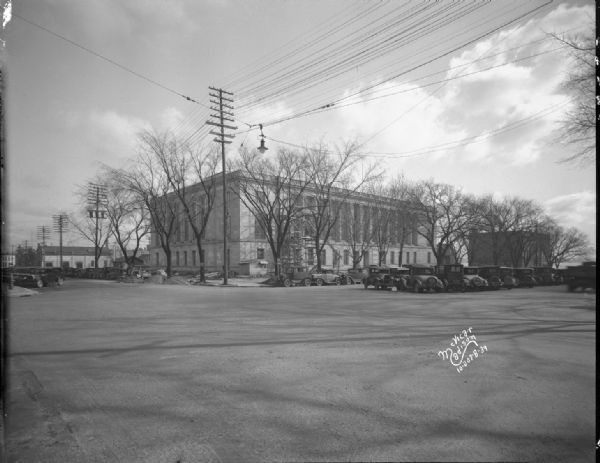 View looking east across intersection towards the nearly completed front and north side of the building. Looking from Doty Street across Monona Avenue with automobiles parked at the curbs and in the median.
