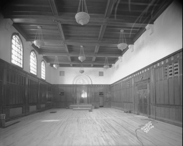 Interior view of empty courtroom showing Judge's platform, paneling, and ceiling with hanging light fixtures.