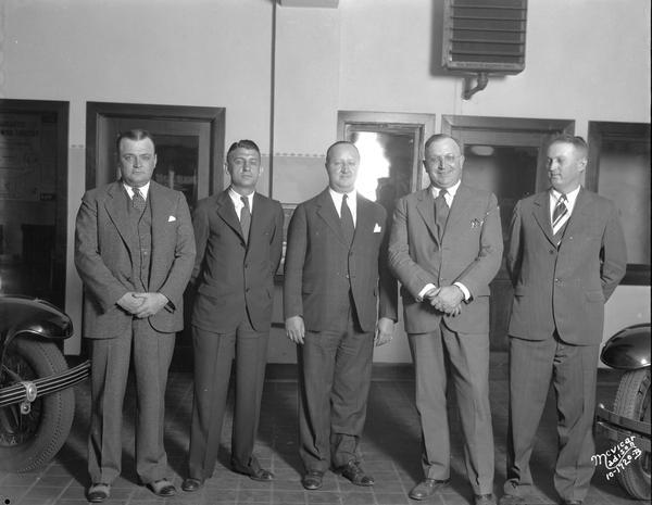 Five Whippet automobile salesmen standing in a row. The front tires of two automobiles are on the left and right.