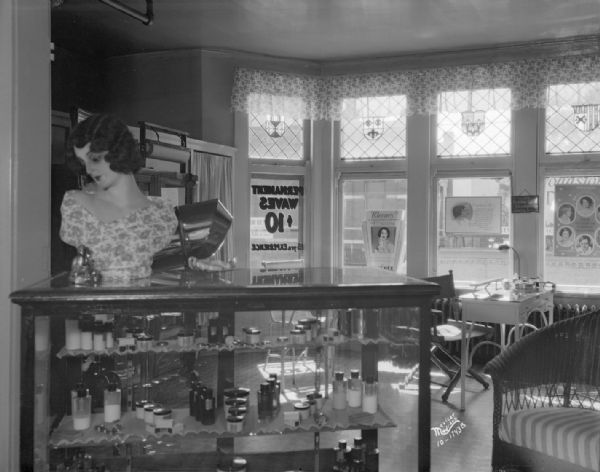 Interior view of the Comfort Beauty Shop, showing display case and advertisements including "Permanent waves $10.00." The front windows are in the background.