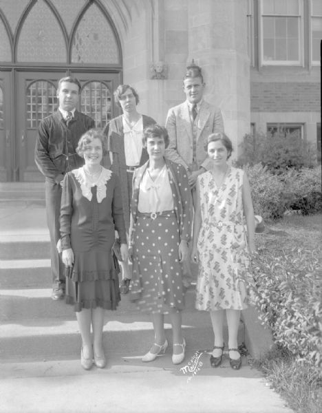 Group portrait of East High School teachers, two men and four women, standing on the steps outside the school.