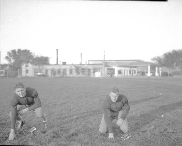 Two Central High School uniformed football players in three point stance on playing field.