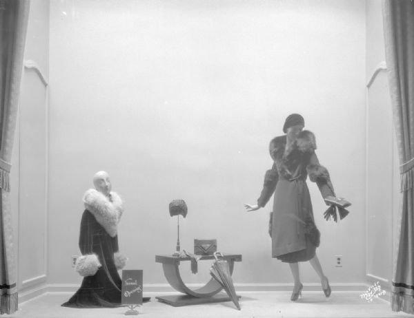 Manchester window display showing two women mannequins wearing hats, and cloth coats with fur trim.