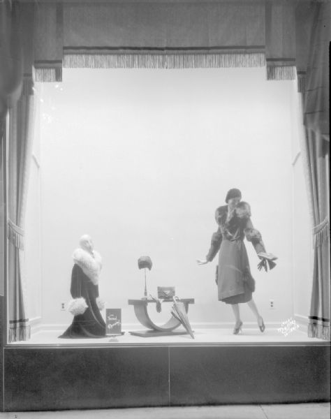 Manchester window display showing two women mannequins wearing hats, and cloth coats with fur trim.
