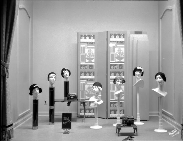 Manchester display window featuring seven mannequin heads with women's hats.