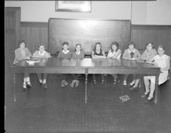 Eight children who were "School page" editors for the "Capital Times," and one adult, sitting around a table.